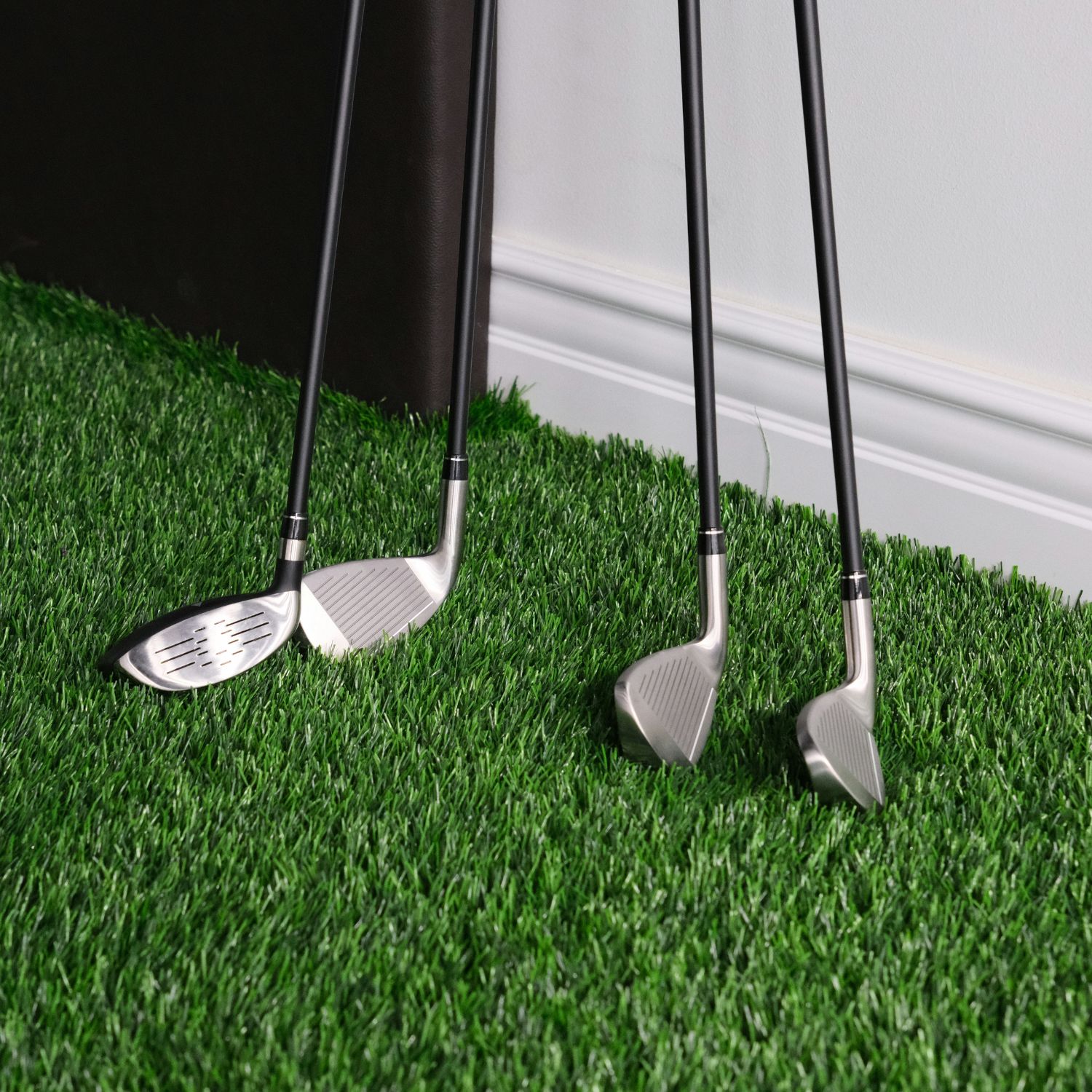 four golf clubs leaning against a wall on golf simulator turf