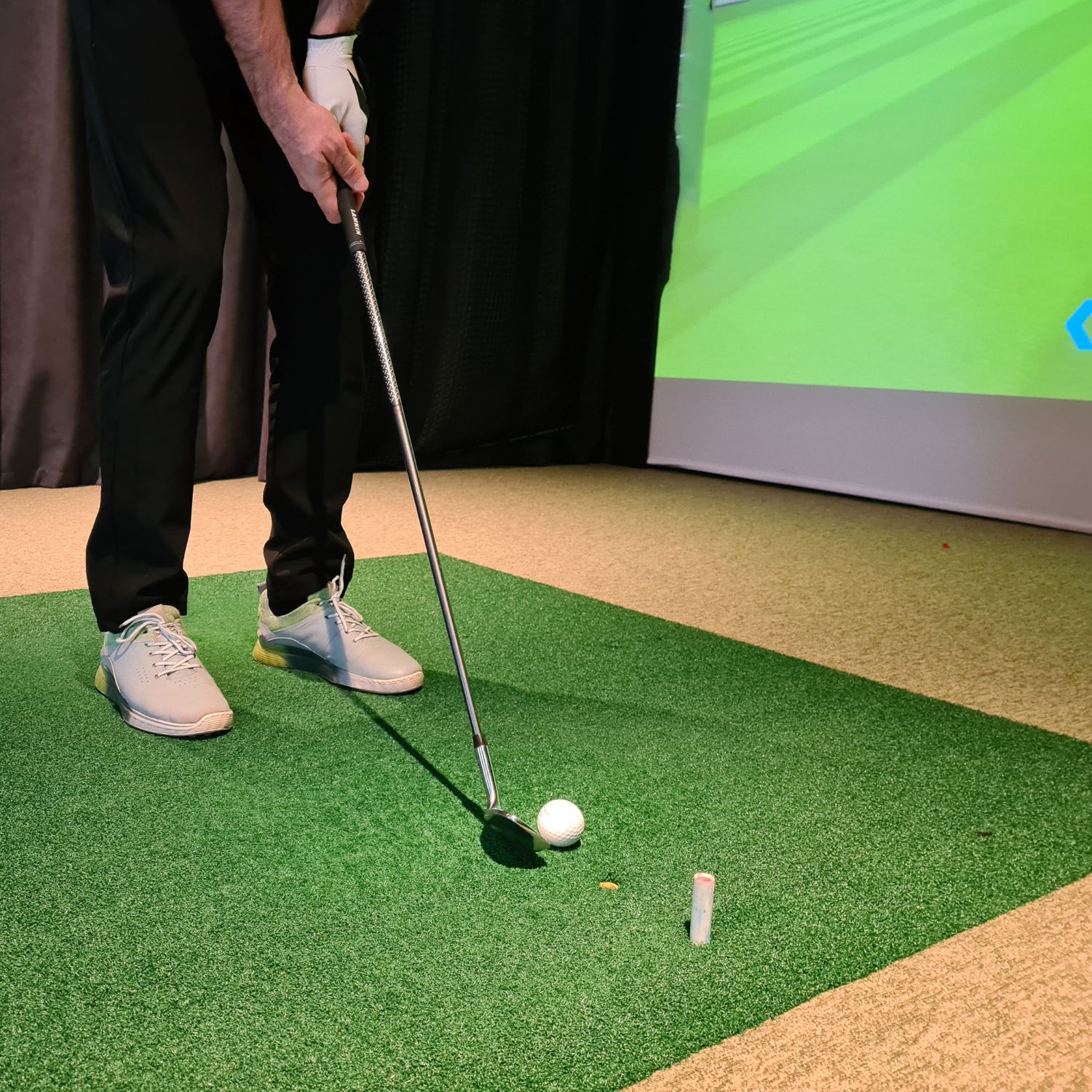Man standing at a golf simulator about to hit the golf ball